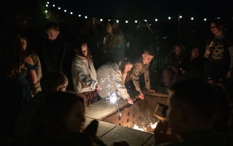 Ashbarton Estate - Wedding guests gather round the fire pit at night at Ash Barton wedding venue Devon