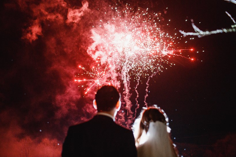 Bride and groom watch red fireworks in night sky at winter wedding venue Ash Barton