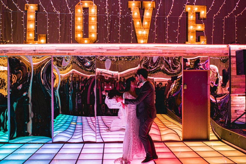 Bride and groom dance in front of wobbly mirrors with pink lights at Ash Barton wedding venue