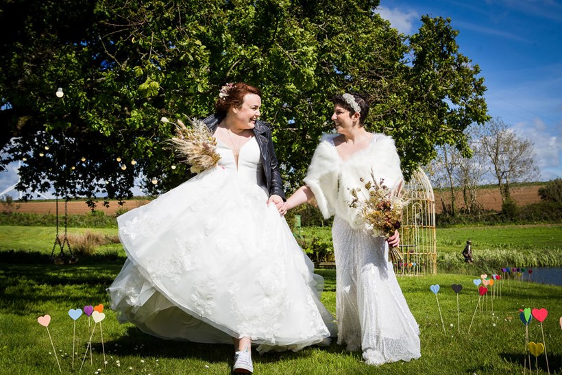 Two brides in wedding dresses hold hands at Ash Barton wedding venue Devon