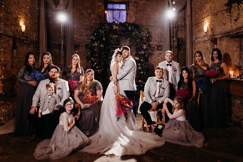 Bride and groom surrounded by guests in moody shot in old chapel at Ash Barton Devon venue